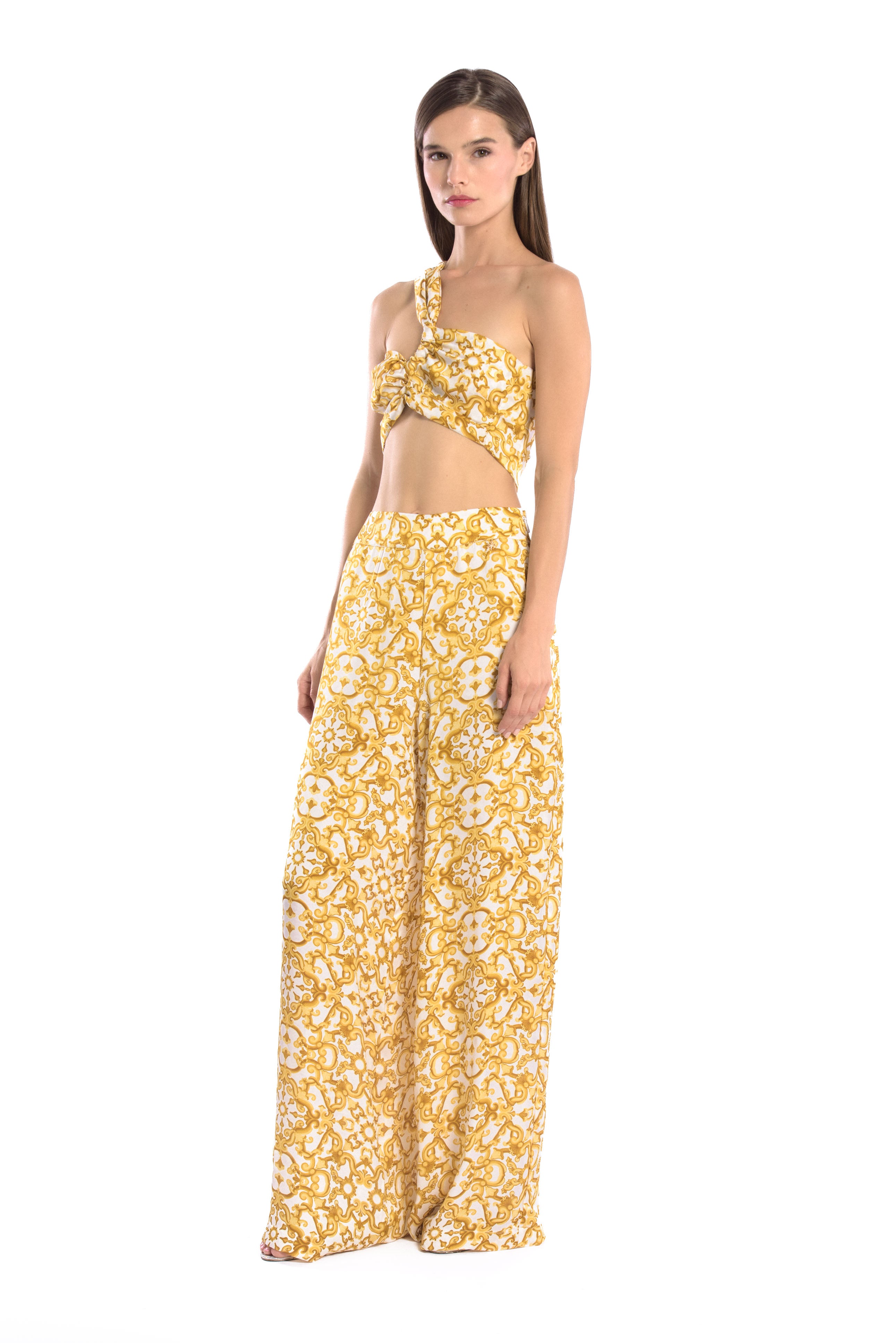 Model wearing a silk cross shoulder crop top in luxury pattern print with back firefly logo golden zipper and silk pants in luxury print pattern with a firefly golden charm