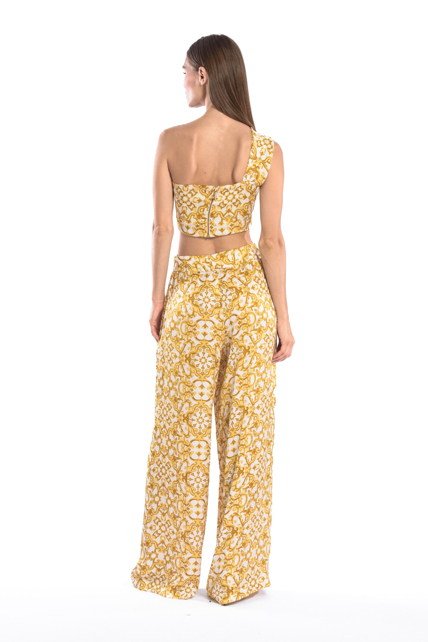 Back shot of model wearing a silk cross shoulder crop top in luxury pattern print with back firefly logo golden zipper and silk pants in luxury print pattern with a firefly golden charm