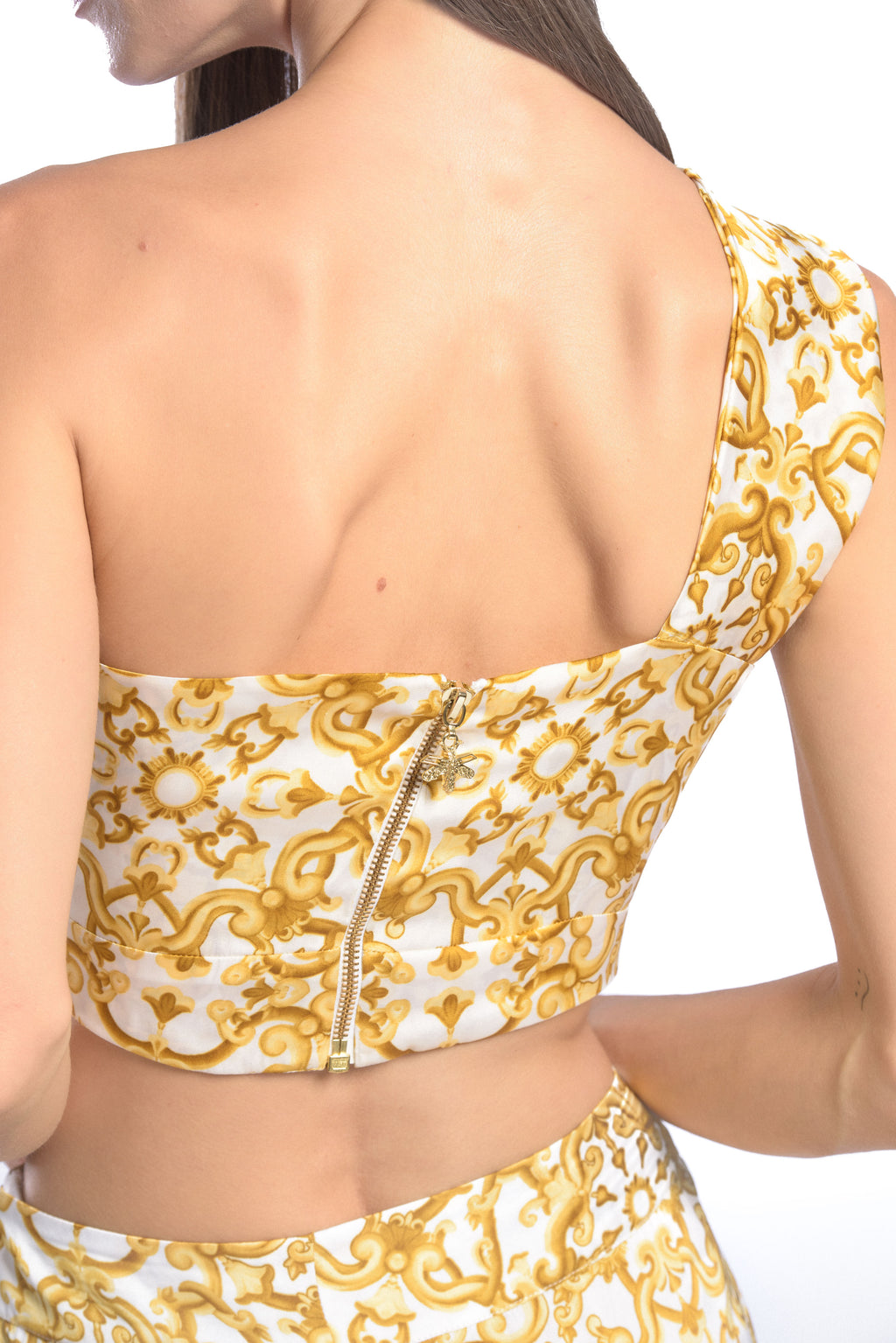 Detail shot of model wearing a silk cross shoulder crop top in luxury pattern print with back firefly logo golden zipper and silk pants in luxury print pattern with a firefly golden charm