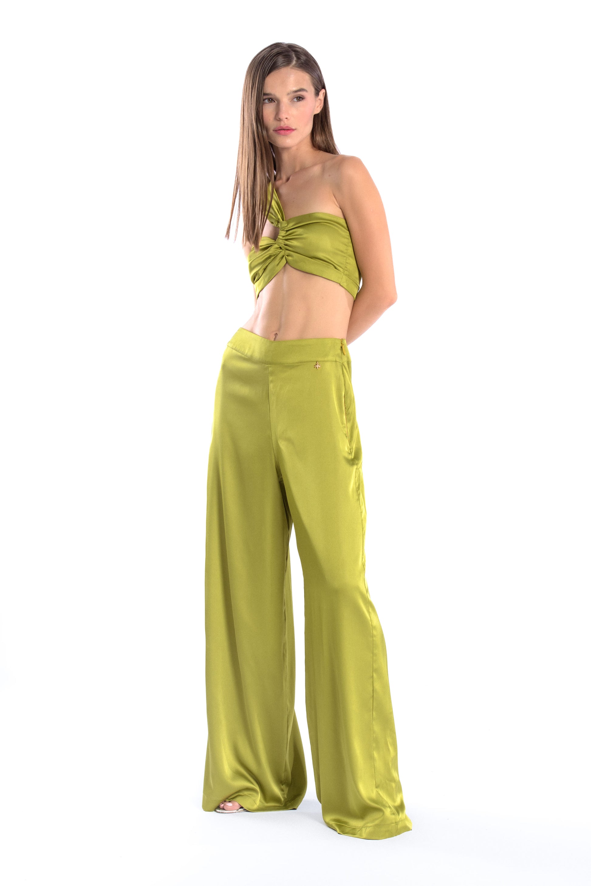 Model wearing a silk cross shoulder crop top in olive with back firefly logo golden zipper and silk pants in olive with a firefly golden charm