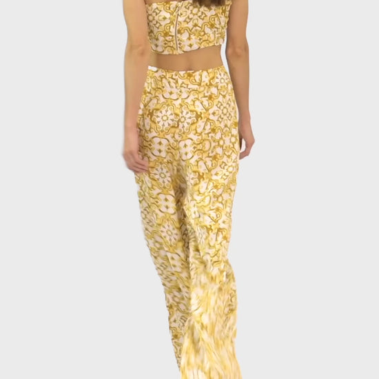 Video of model wearing a silk cross shoulder crop top in luxury pattern print with back firefly logo golden zipper and silk pants in luxury print pattern with a firefly golden charm