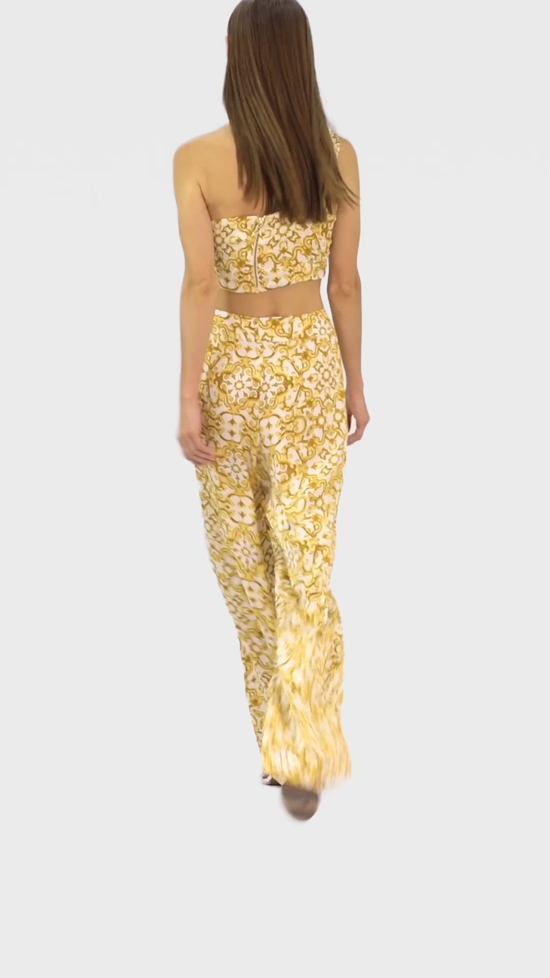 Video of model wearing a silk cross shoulder crop top in luxury pattern print with back firefly logo golden zipper and silk pants in luxury print pattern with a firefly golden charm