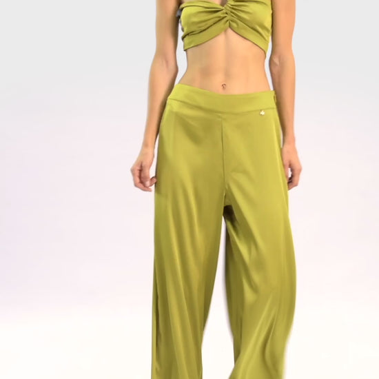 Video of model wearing a silk cross shoulder crop top in olive with back firefly logo golden zipper and silk pants in olive with a firefly golden charm on white background